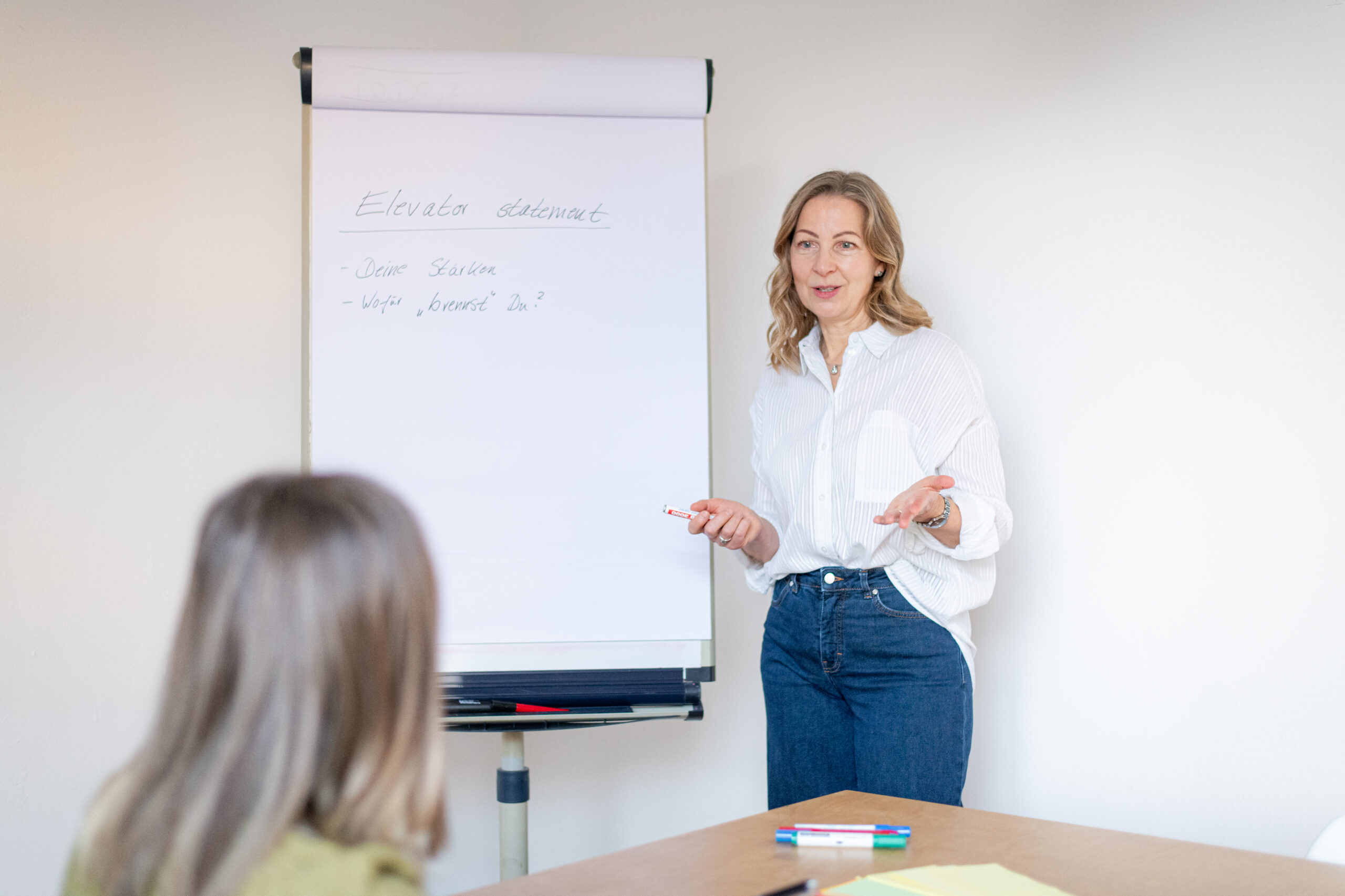 Silke steht an einem Flipchart und erklärt einer Klientin etwas.