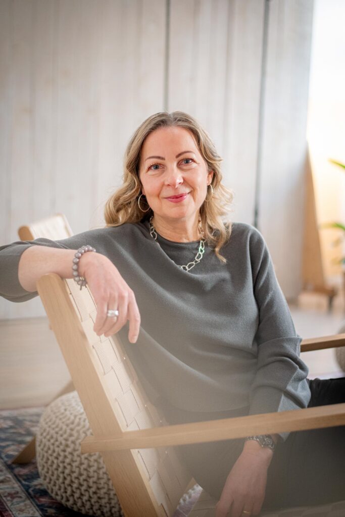 Silke sitzt lächelnd auf Stuhl, Arm über der Lehne