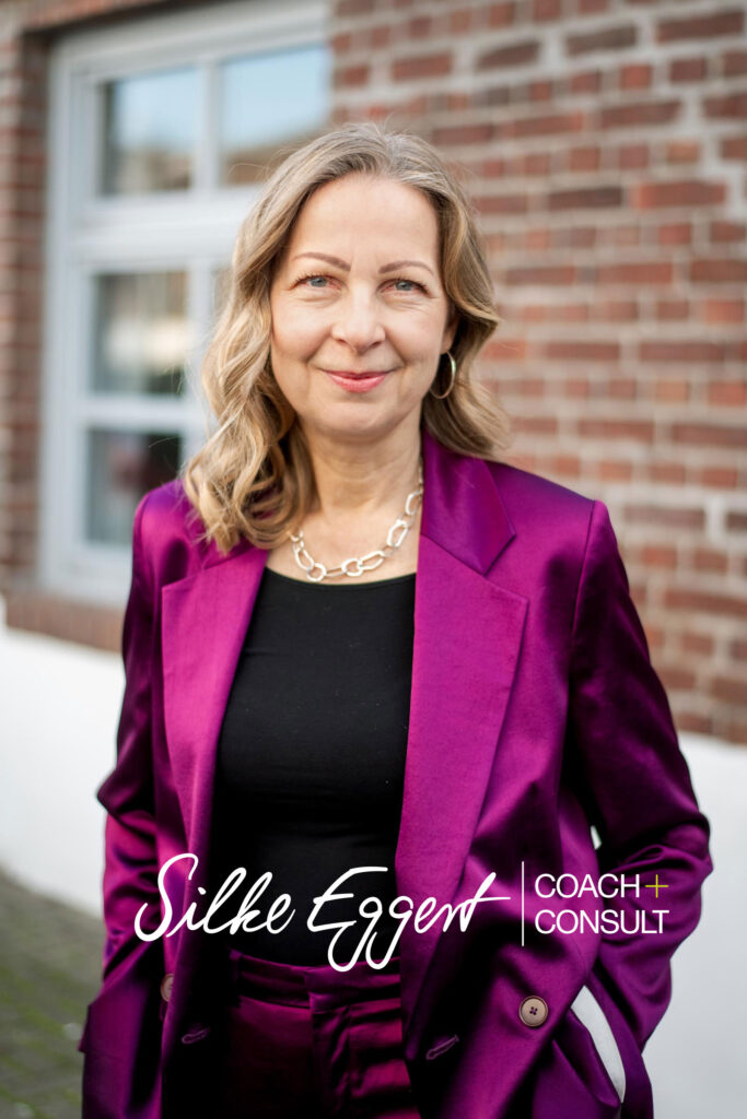 Silke is standing in front of a wall dressed in a purple blazer